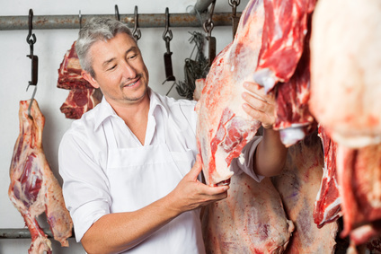 Confident mature male butcher checking quality of meat hanging in butchery